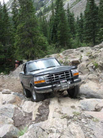 1995 Ford Bronco - Black Ford Bronco driving off-road through a rocky mountain pass.