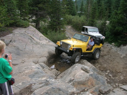 1995 Ford Bronco - Two Jeeps tackle a challenging off-road course in a mountainous, wooded area.