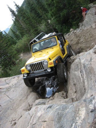 1995 Ford Bronco - A yellow Jeep Wrangler navigates a rocky trail, with a person watching from a high rock.