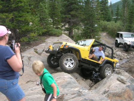 1995 Ford Bronco - A yellow Jeep Wrangler tackles a challenging rocky trail, with a white Jeep following behind.