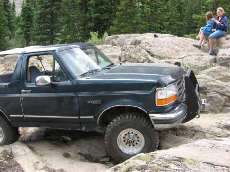 1995 Ford Bronco - Ford Bronco on a rocky trail with two people sitting on rocks in the background.