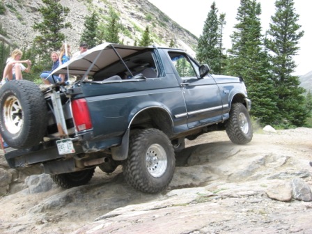 1995 Ford Bronco - A dark blue Ford Bronco navigates a rocky mountain trail with passengers enjoying the ride.