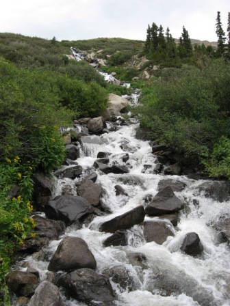 1995 Ford Bronco - A rushing mountain stream flows downhill over a rocky bed, surrounded by lush green vegetation.