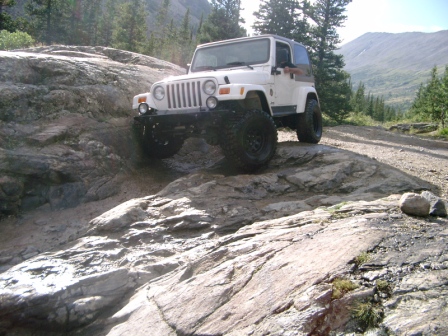 1995 Ford Bronco - White Jeep Wrangler TJ navigating a challenging rocky trail in a mountainous area.