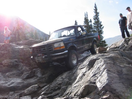 1995 Ford Bronco - A 1995 Ford Bronco navigates a rocky mountain path under a bright sun.