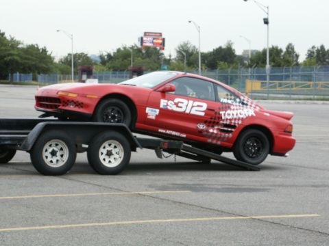 2001 Mercury Grand Marquis - A red Toyota MR2, marked with racing graphics, is being transported on a trailer.