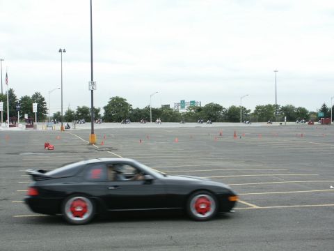 2001 Mercury Grand Marquis - A black sports car with distinctive red wheels navigates a course marked by orange cones in a large parking lot.