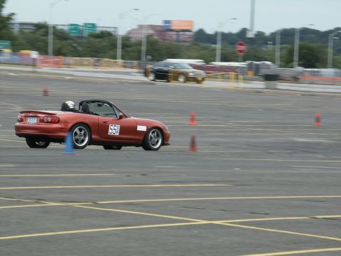 2001 Mercury Grand Marquis - A red convertible sports car navigates a course marked by traffic cones, with another vehicle blurred in the background.