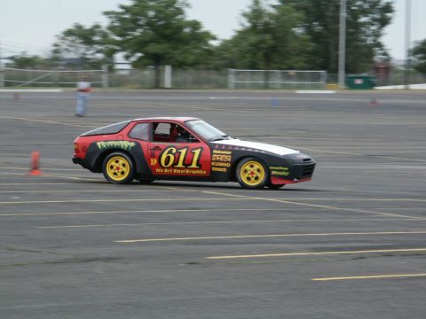 2001 Mercury Grand Marquis - A red and black sports car with yellow wheels and racing decals navigates a track, indicated by orange cones.