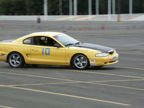 2001 Mercury Grand Marquis - A yellow Ford Mustang with a black hood is seen on a race track, participating in an event.