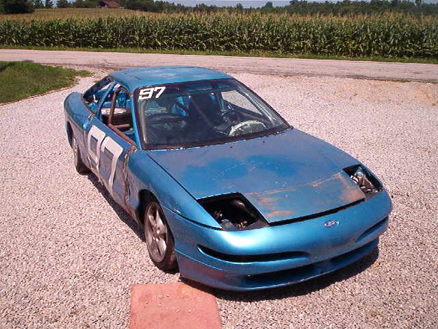 Blue 1993 Ford Probe race car with number 97 on door and windshield banner, parked on gravel
