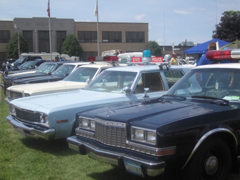 1991 Ford LTD Crown Victoria - row of classic police sedans, one labeled STATE POLICE with a roof light, lines up on grass before a two-story brick building.