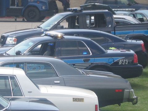 1991 Ford LTD Crown Victoria - tightly packed row of police cars with roof lightbars, including a SHERIFF unit and a blue DIAL 9-1-1 cruiser, seen at close range.