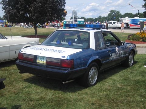1991 Ford LTD Crown Victoria - blue-and-white Ford Mustang notchback marked Georgia State Patrol sits on grass with lightbar at an outdoor police car show.