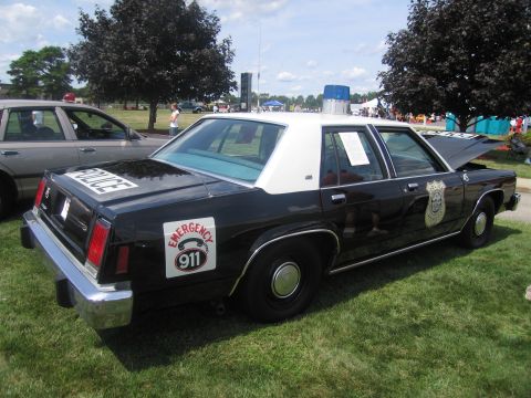 1991 Ford LTD Crown Victoria - black-and-white Ford LTD Crown Victoria police sedan with POLICE and Emergency 911 markings displayed on grass at a car show.