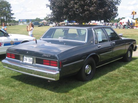 1991 Ford LTD Crown Victoria - dark blue Chevrolet Biscayne full-size sedan with police-style markings parked on grass among other cruisers at a show.