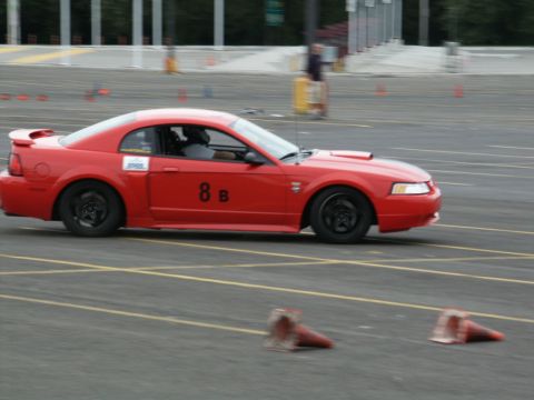 2001 Mercury Grand Marquis - A red coupe, possibly a Ford Mustang, navigates a course marked by cones during a motorsports event.
