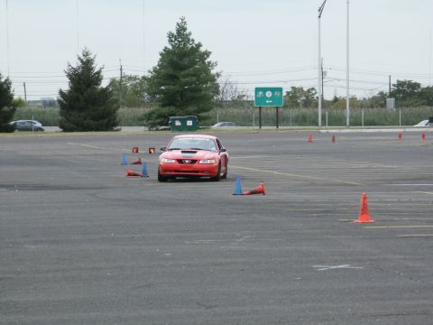 2001 Mercury Grand Marquis - A red sports car drives through a cone course on a paved lot.