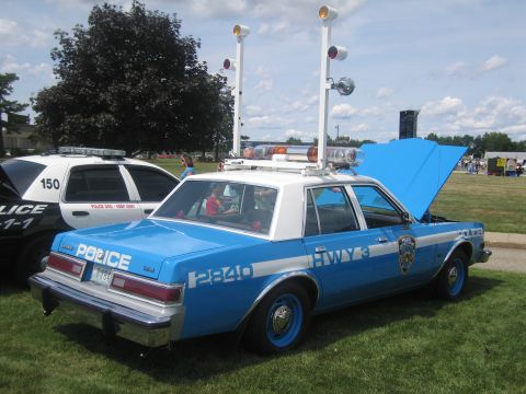 1991 Ford LTD Crown Victoria - blue-and-white NYPD Highway Patrol Plymouth police sedan loaded with rooftop lights and speakers on grass at a car show.
