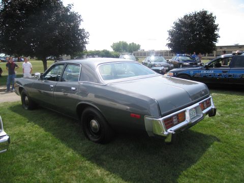1991 Ford LTD Crown Victoria - gray two-tone full-size 1970s sedan parked on grass at a car show, with police cruisers in the background.