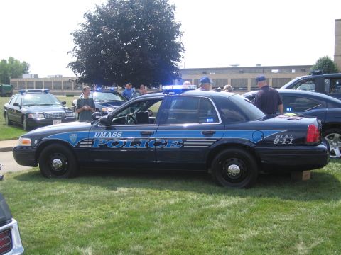 1991 Ford LTD Crown Victoria - black UMass Police Ford Crown Victoria cruiser with blue striping and Dial 9-1-1 lettering displayed on grass at a car show.