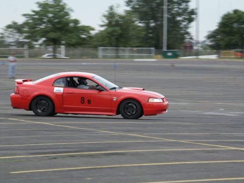 2001 Mercury Grand Marquis - Red Ford Mustang with racing numbers on the door navigates an asphalt track.