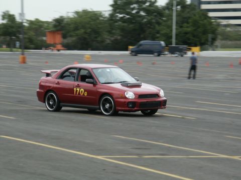 2001 Mercury Grand Marquis - A red Subaru Impreza WRX participates in an event on a paved lot marked with cones.