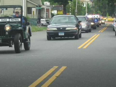 1991 Ford LTD Crown Victoria - green vintage Jeep marked Park Patrol leads a sedan and emergency vehicles with flashing lights down a residential road.