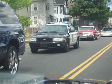 1991 Ford LTD Crown Victoria - black-and-white Ford Crown Victoria police cruiser marked 125 drives down a road in a parade of classic cars.