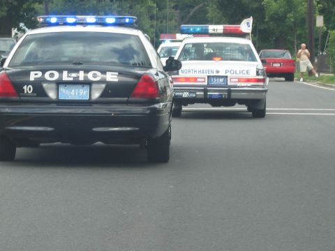 1991 Ford LTD Crown Victoria - rear of a black police cruiser with blue roof lights sits beside a white North Haven Police car on a street.