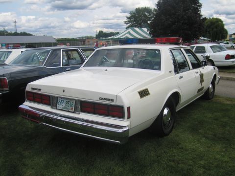 1991 Ford LTD Crown Victoria - Rear-quarter view of a white Chevrolet Caprice sheriff cruiser with roof lightbar and plate 242 8516, parked on grass with other cars at a…