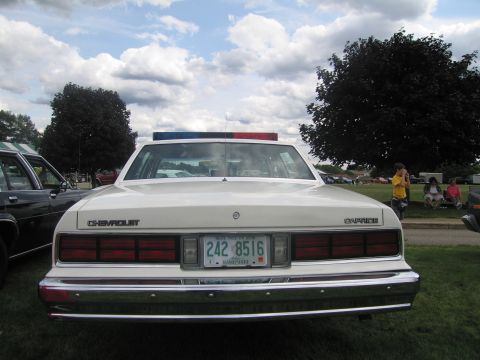 1991 Ford LTD Crown Victoria - Head-on front view of a white Chevrolet Caprice police car with a red-and-blue roof lightbar and New Hampshire plate 242 8516, on grass und…