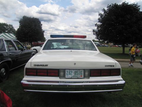 1991 Ford LTD Crown Victoria - Rear head-on view of a white Chevrolet Caprice police cruiser with roof lightbar and New Hampshire plate 242 8516, parked on grass at a car…