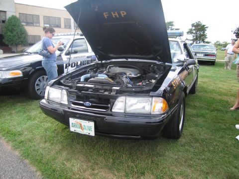 1991 Ford LTD Crown Victoria - Black Ford Mustang Florida Highway Patrol state trooper car with its hood raised, showing 'FHP' on the hood and a green 'Arrive Alive' Flor…