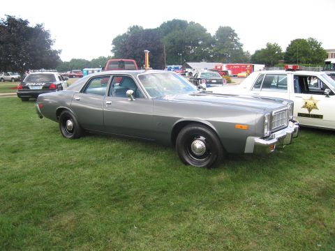 1991 Ford LTD Crown Victoria - Side-front view of a gray late-1970s Dodge four-door police sedan on grass, with other police cars and trucks in the background at a show.