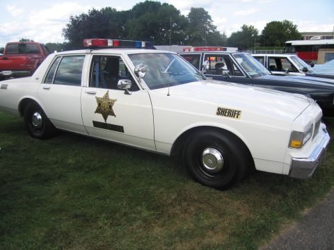 1991 Ford LTD Crown Victoria - Side-front view of a white Chevrolet Caprice sheriff cruiser with a gold star door decal, 'SHERIFF' lettering and roof lightbar, parked on…