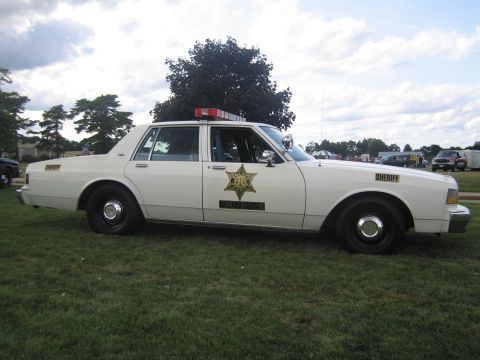 1991 Ford LTD Crown Victoria - Full side profile of a white Chevrolet Caprice four-door sheriff sedan with a gold star door decal, 'SHERIFF' lettering and roof lightbar,…