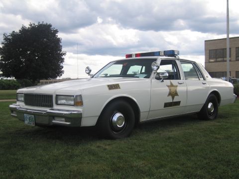 1991 Ford LTD Crown Victoria - Front-three-quarter view of a white Chevrolet Caprice sheriff sedan with a gold star door decal, 'SHERIFF' lettering, spotlight and roof li…