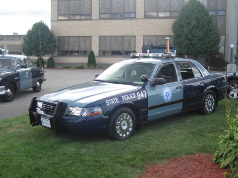 1991 Ford LTD Crown Victoria - blue-and-gray Massachusetts State Police Ford Crown Victoria cruiser numbered 947 parked on grass beside a brick building.