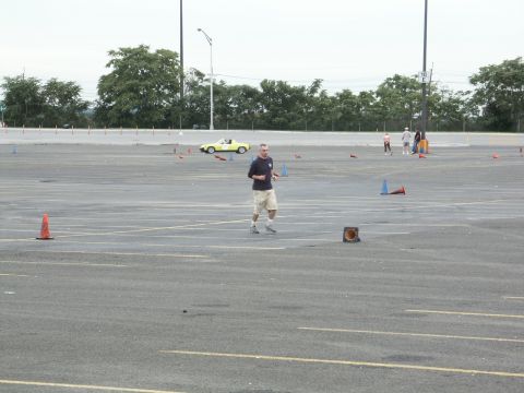2001 Mercury Grand Marquis - A man runs through a parking lot set up for an autocross event with cones and a yellow car visible.