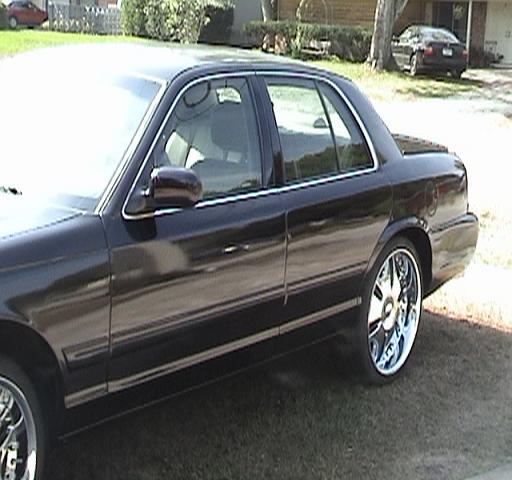 Side profile of a dark Mercury sedan on chrome rims in a driveway