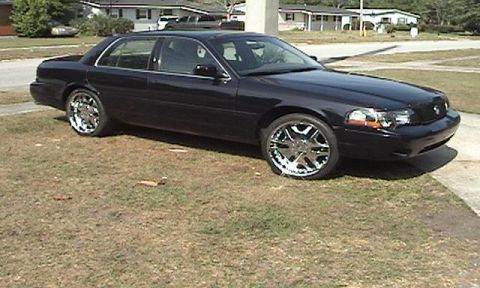 1998 Ford Crown Victoria - This black sedan, likely a Mercury Grand Marquis from the early 2000s, is parked on a grassy area.