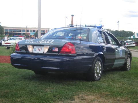 1991 Ford LTD Crown Victoria - Rear three-quarter view of a dark State Police Ford Crown Victoria numbered 947 with roof light bar displayed on a lawn.