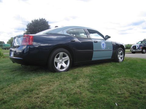 1991 Ford LTD Crown Victoria - dark blue Dodge Charger police car with state seal door decal and number 492, viewed from the rear quarter on grass.