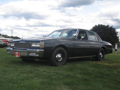 1991 Ford LTD Crown Victoria - black Chevrolet Caprice sedan with chrome trim and a Canadian flag plate displayed on a grassy field at a show.