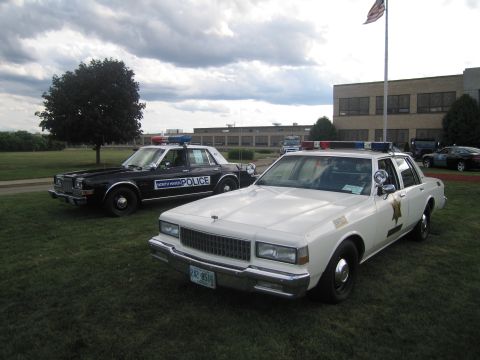 1991 Ford LTD Crown Victoria - white sheriff's cruiser and a black-and-white North Haven Police sedan sit side by side on a lawn under cloudy skies.