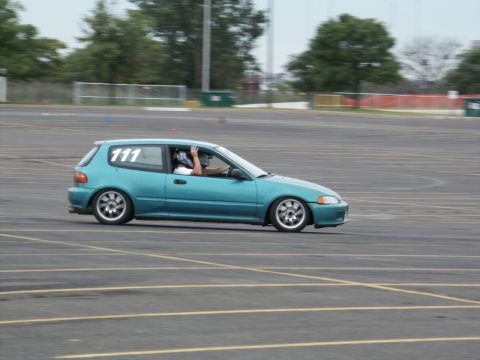 2001 Mercury Grand Marquis - A teal hatchback with racing number 111 on the window navigates a course on a paved lot.
