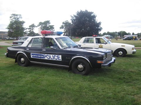 1991 Ford LTD Crown Victoria - black-and-white North Haven Police sedan with roof lightbar parked front-quarter on a grassy field with other cars behind.