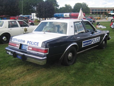 1991 Ford LTD Crown Victoria - Rear three-quarter view of a black-and-white North Haven Police sedan with a small flag, parked on a grassy show field.