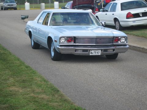 1991 Ford LTD Crown Victoria - light blue four-door sedan with chrome grille drives along a paved lot past other parked vehicles.